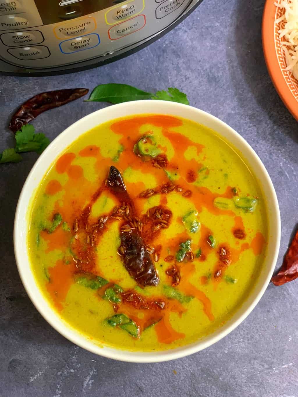 instant pot palak kadhi recipe in a white bowl and instant pot on side with red chillies for decoration