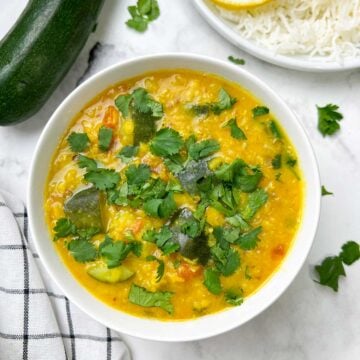 zucchini dal served in a bowl garnished with cilantro and side of steamed rice