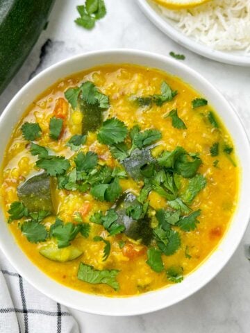 zucchini dal served in a bowl garnished with cilantro and side of steamed rice