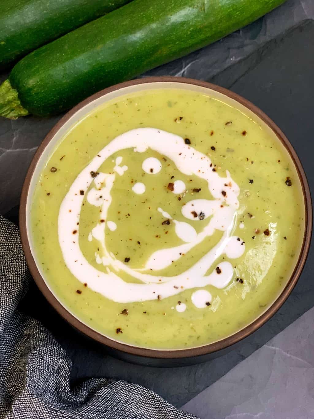 courgette soup served in a bowl and two raw zucchini on the side