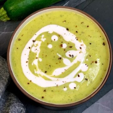 Zucchini Soup served in a bowl topped with cream and pepper and whole zucchini on side