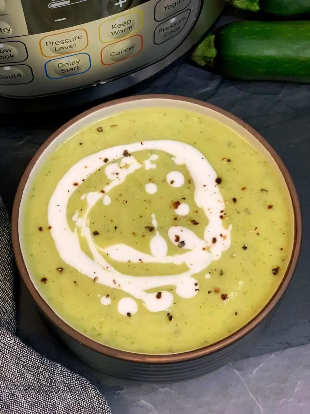 zucchini soup served in a bowl topped with cream and black pepper and instant pot on the side