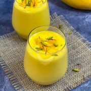 Mango lassi served in a serving glass topped with pistachios and saffron