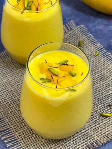 Mango lassi served in a serving glass topped with pistachios and saffron