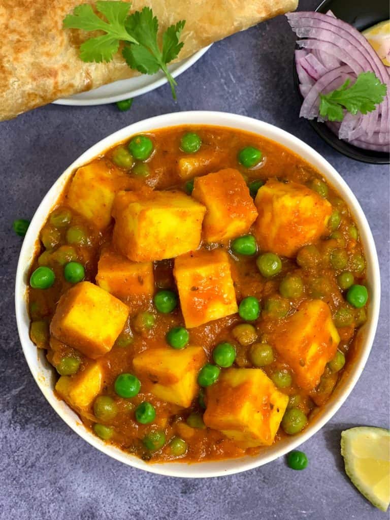 matar paneer served in a bowl with paratha onions and lemon wedge on the side