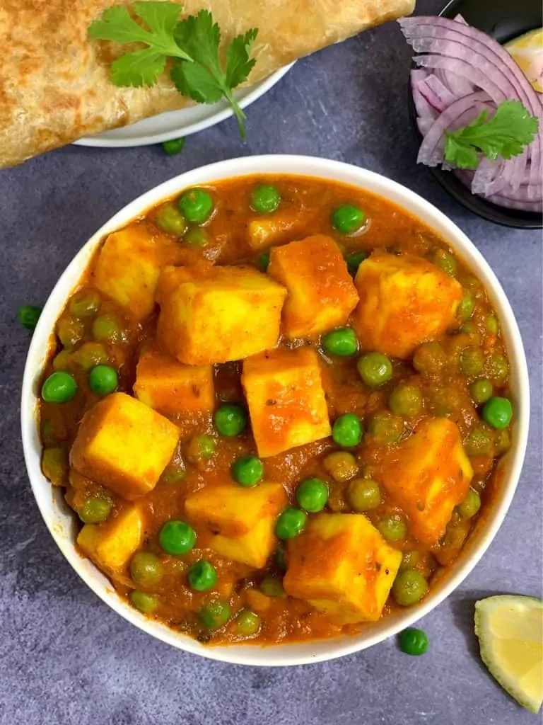 matar paneer served in a bowl with paratha onions and lemon wedge on the side