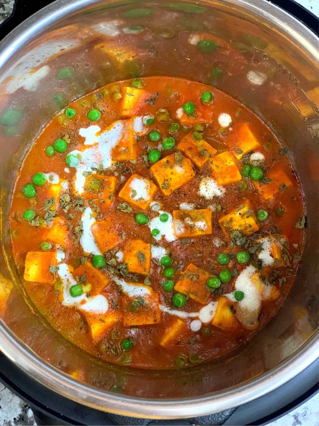 mutter paneer in instant pot insert garnished with cream and cilantro