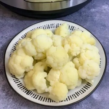 Steamed Cauliflower served in a plate and instant pot on the side