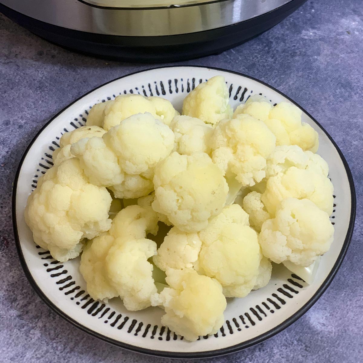 Steamed Cauliflower served in a plate and instant pot on the side