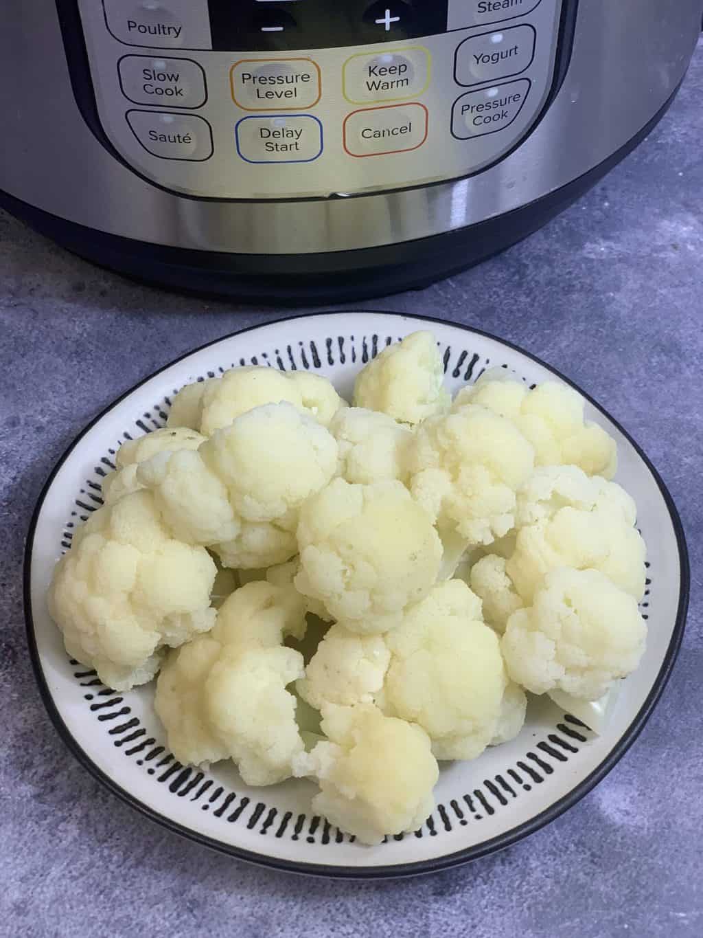 Steamed Cauliflower in a plate with instant pot on the side