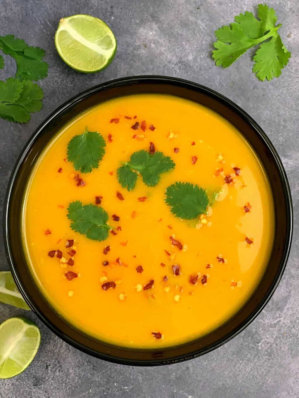 Instant pot pumpkin thai curry soup in a black bowl and lemon wedges on the side