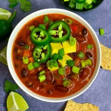Vegetarian Chili served in a white bowl garnished with jalapeños avocado and green onions