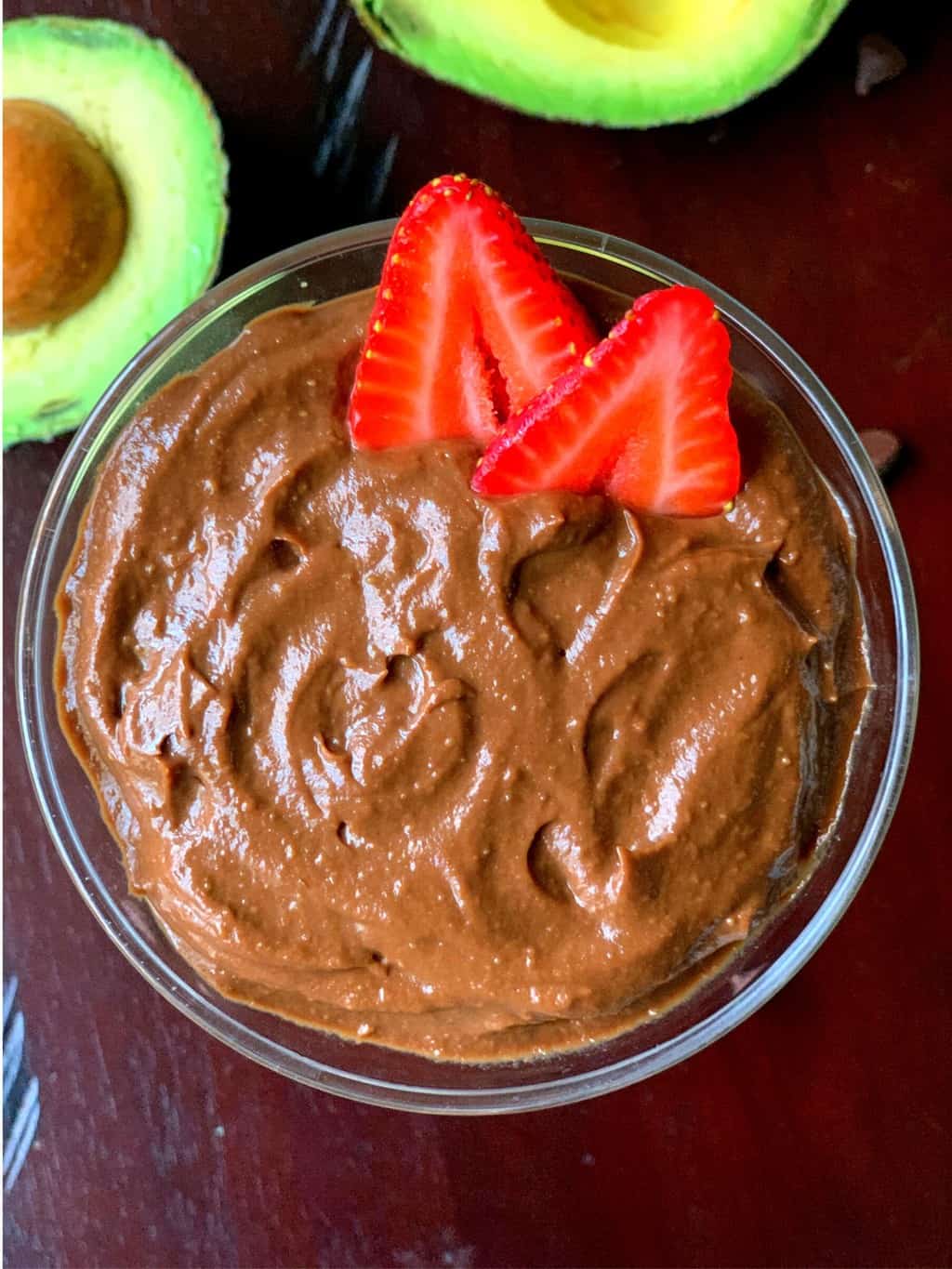avocado chocolate mousse in a glass bowl with strawberries on top and avocados on side for garnish