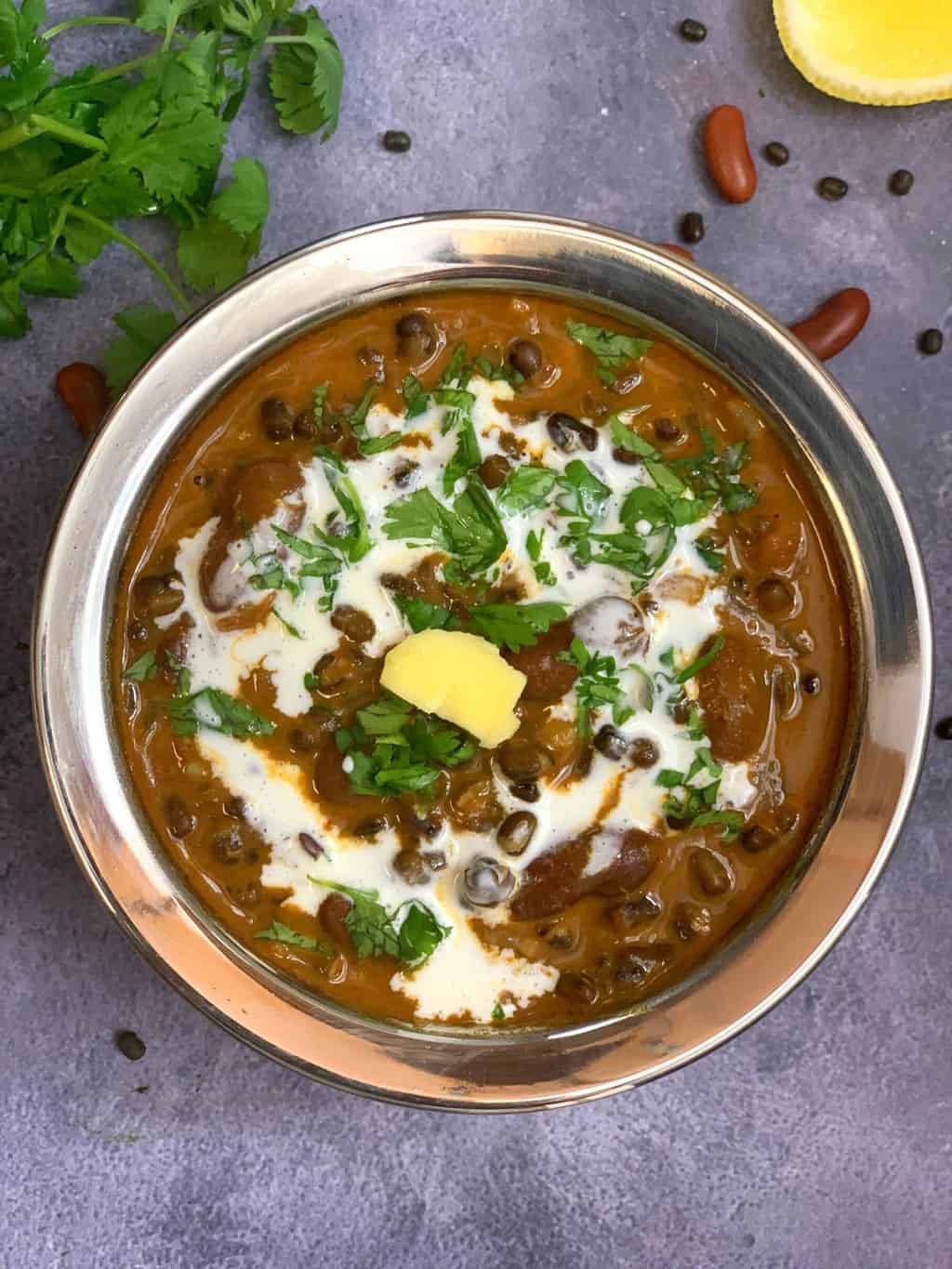 instant pot dal makhani in a copper bottom bowl with cream and butter on top and with cilantro dry beans on side for garnish