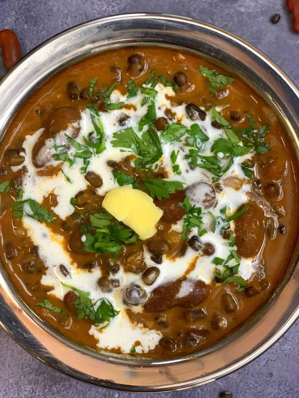 dal makhani served in a steel vessel topped with cream butter and cilantro