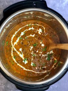 dal makhani in instant pot insert with a wooden spoon and garnished with cream and cilantro