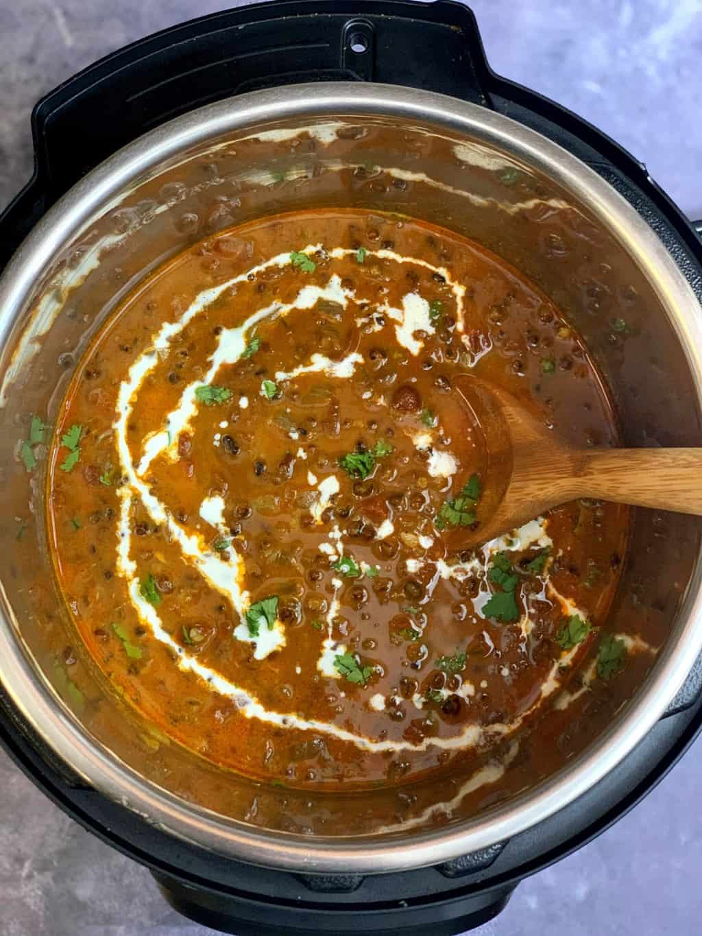 dal makhani in instant pot insert with a wooden spoon and garnished with cream and cilantro