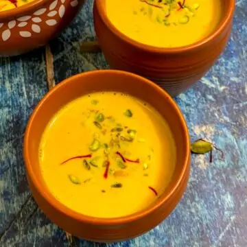 Carrot almond kheer served in a mud pot garnished with pistachios and saffron stands