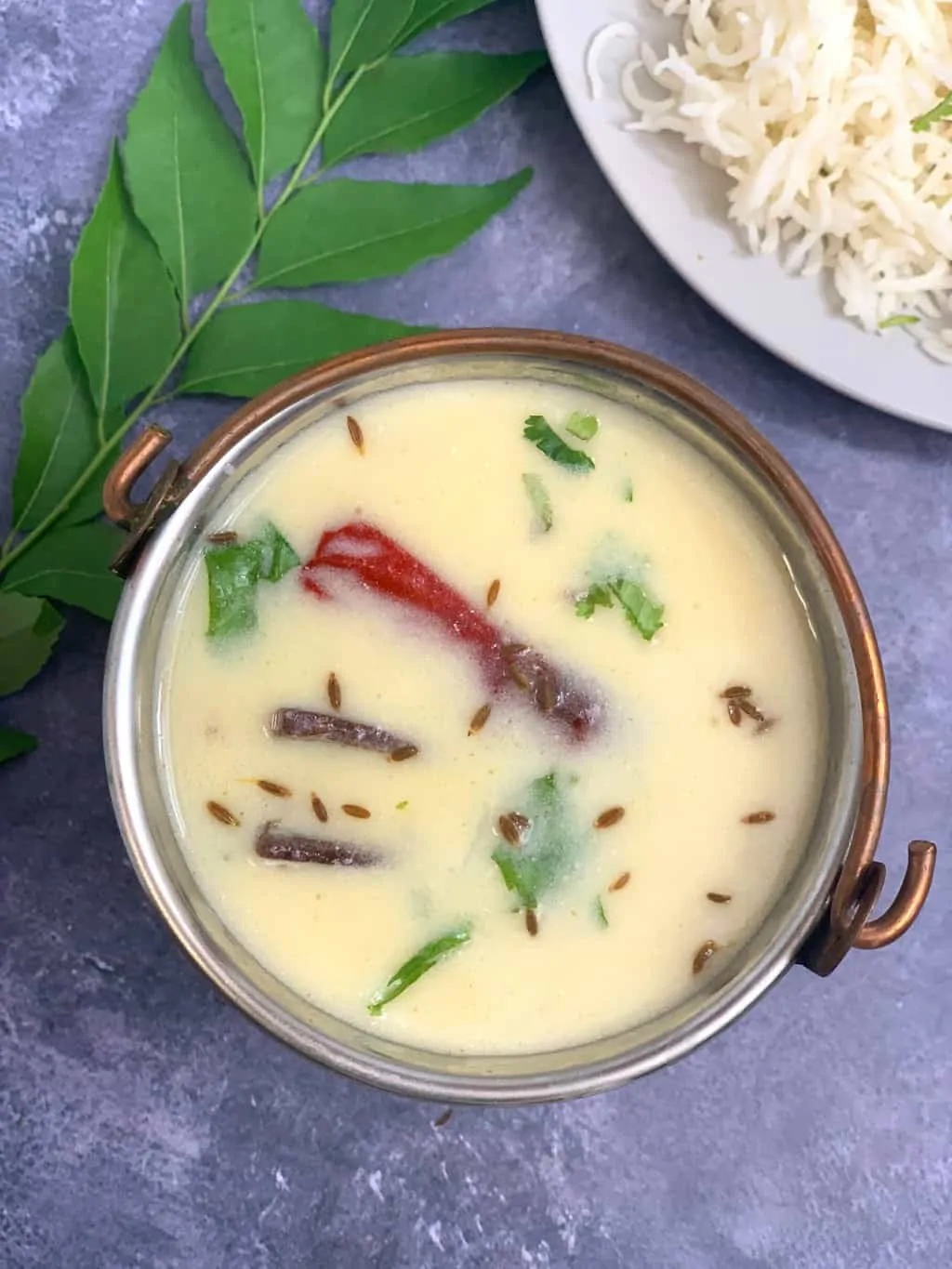instant pot gujarati kadhi in a copper bowl with side of rice and curry leaves