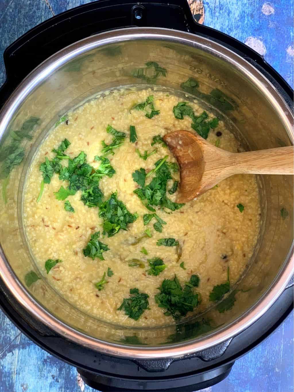pressure cooker foxtail millet healthy pongal in the instant pot insert with a wooden spoon garnished with cilantro 