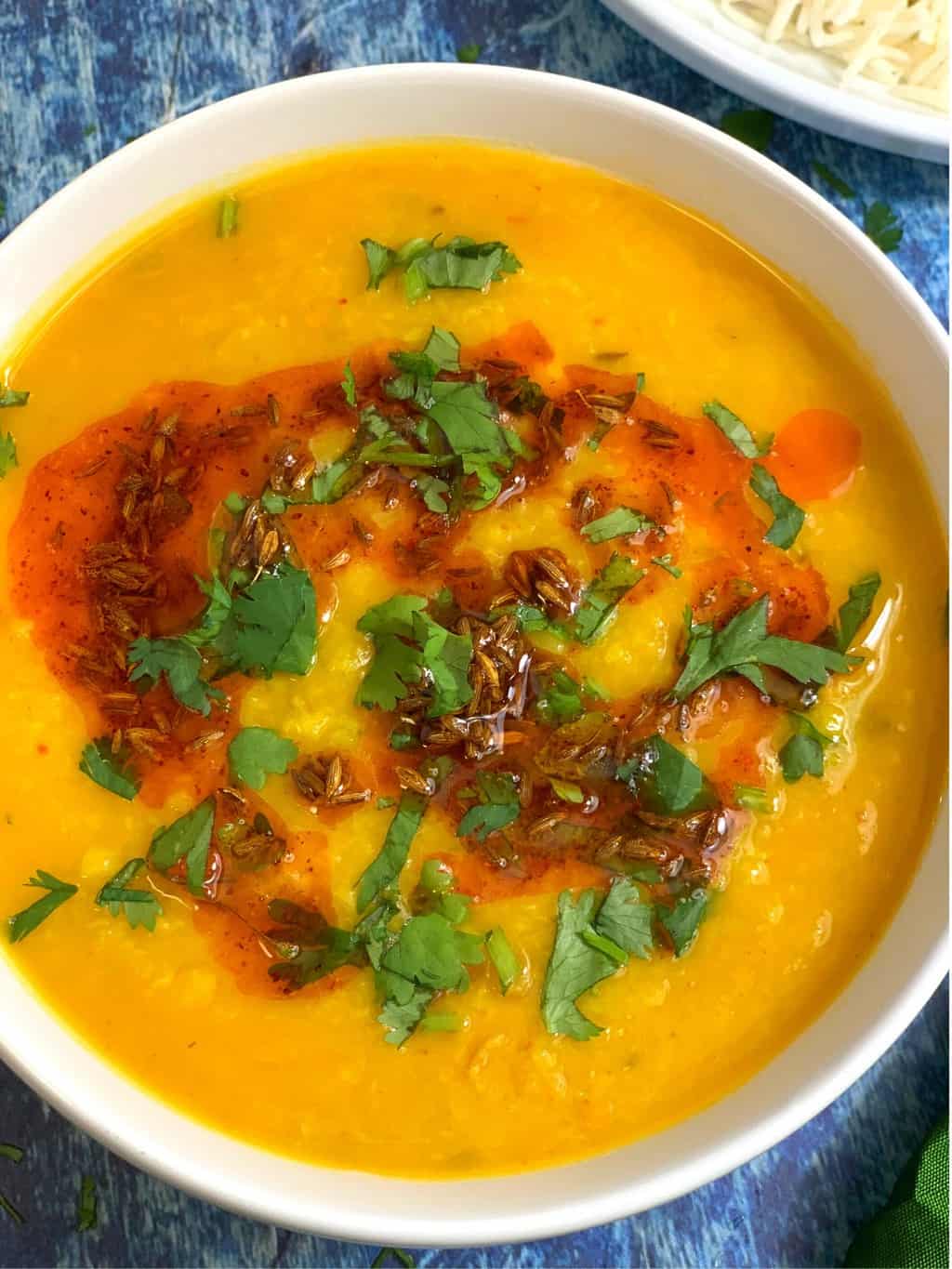 yellow lentil soup served in a bowl garnished with cilantro and tempering on the top