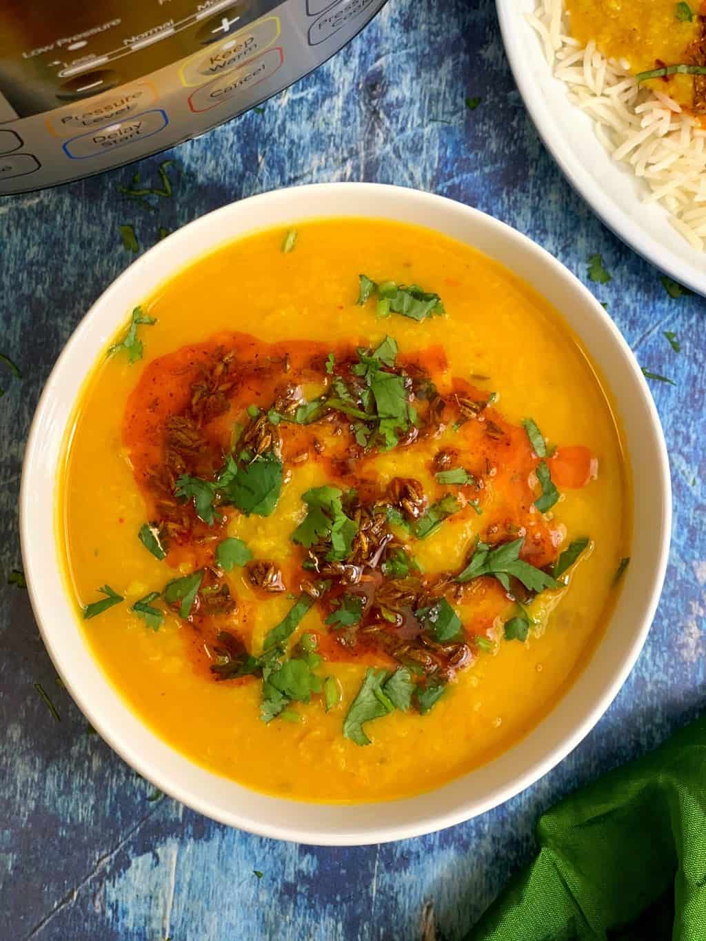 moong dal tadka with tempering on top served in a white bowl ,rice with dal served in a plate on side.