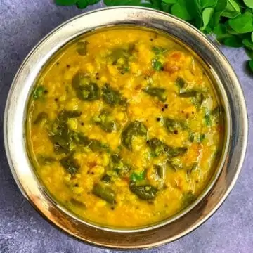 Moringa Leaves Dal served in a steel bowl with fresh moringa leaves on side