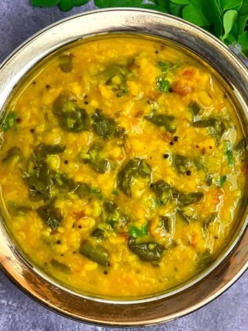 Moringa Leaves Dal served in a steel bowl with fresh moringa leaves on side