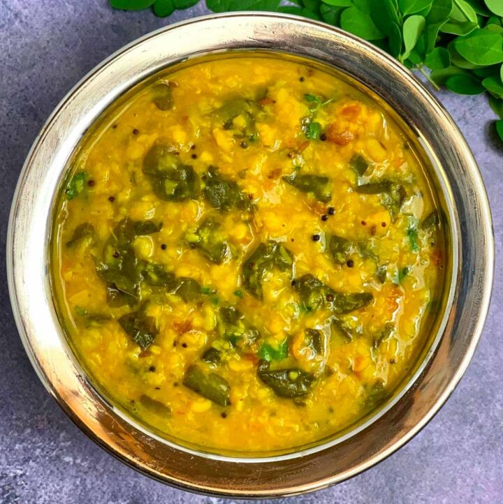 Moringa Leaves Dal served in a steel bowl with fresh moringa leaves on side