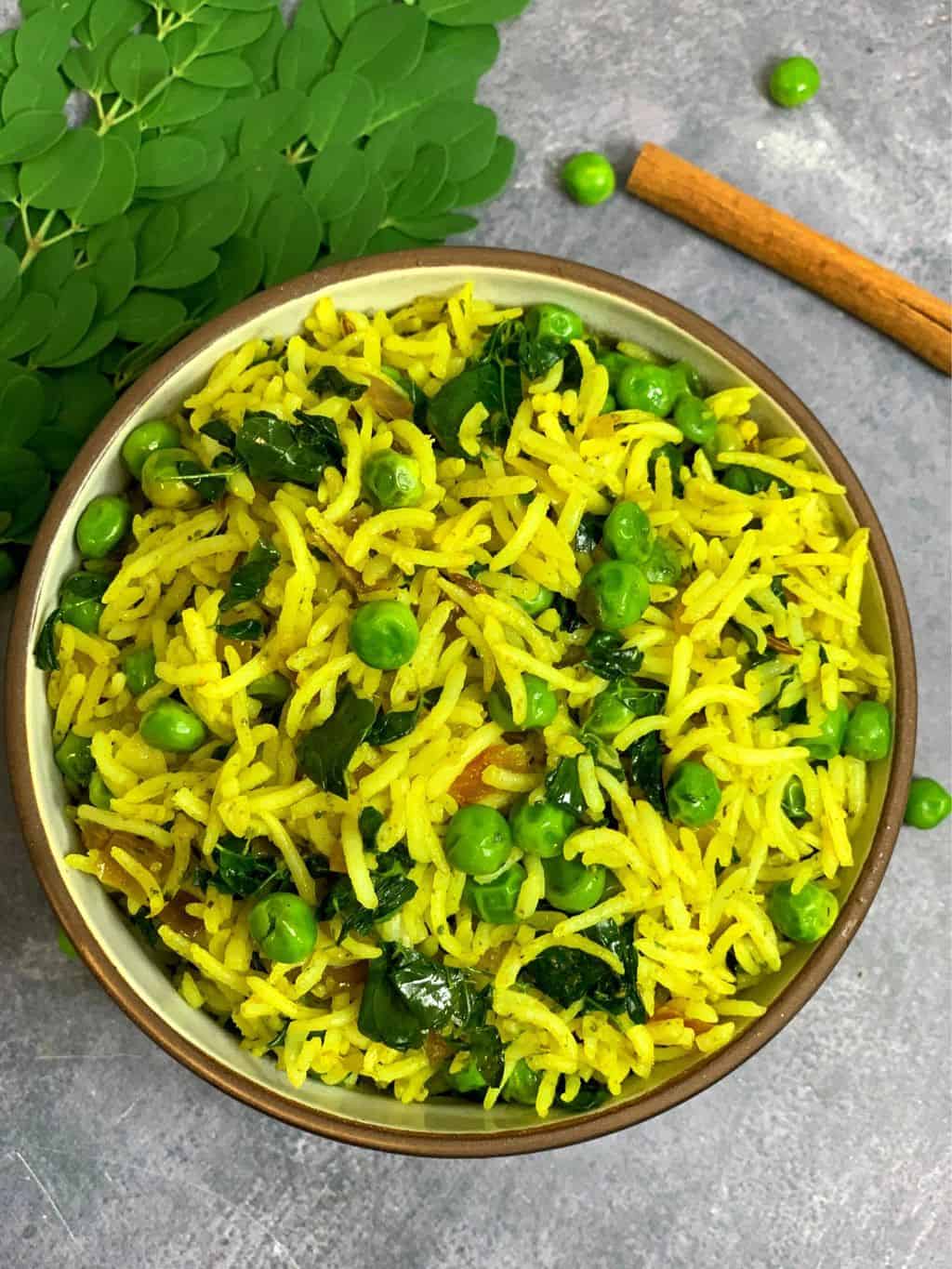 superfood moringa/drumstick leaves rice served in a bowl and drumstick leaves ,peas and cinnamon stick on side