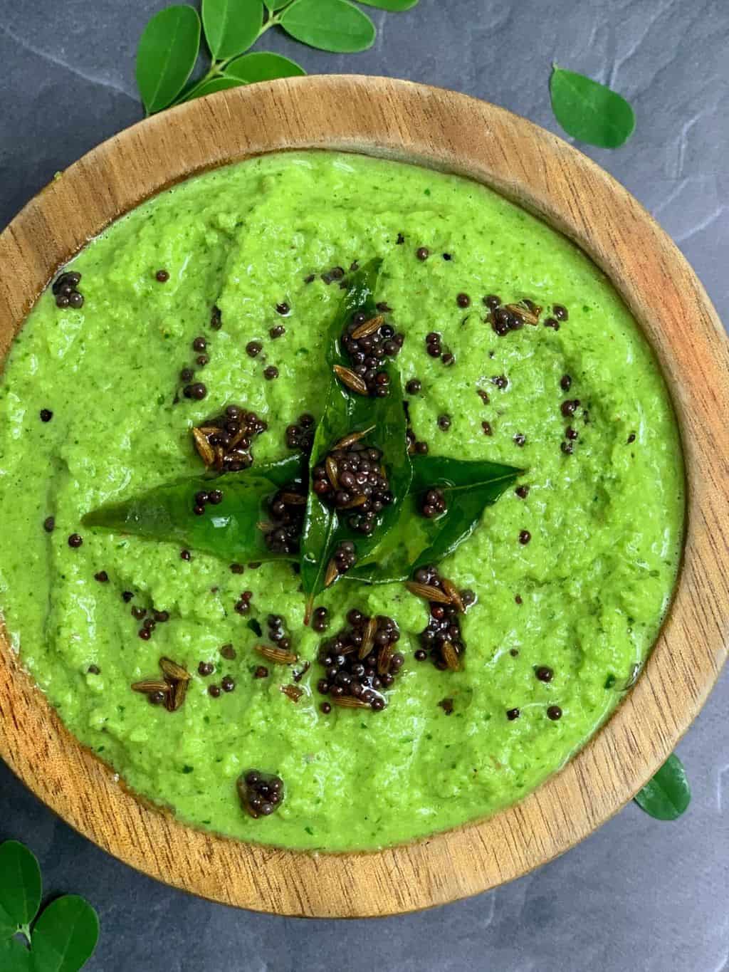 drumstick leaves coconut chutney served in a wooden bowl with tempering on the top