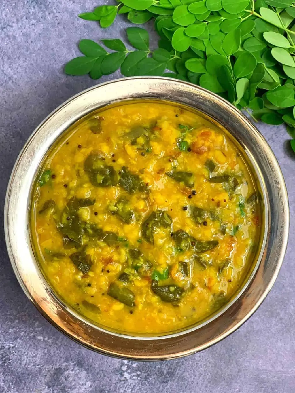 Moringa leaves moong dal in a steel bowl with drumstick leaves on side