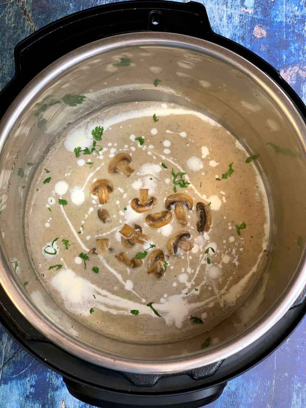 creamy mushroom soup in instant pot insert topped with cream cilantro and sauteed mushrooms