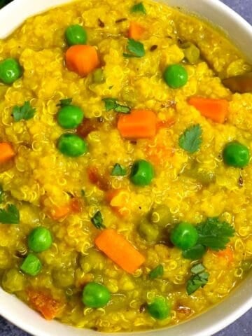 Quinoa Vegetable Khichdi served in a white bowl with green peas and carrot on top