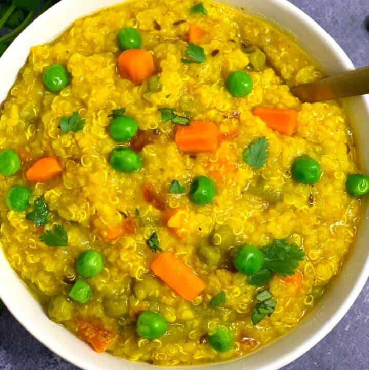 Quinoa Vegetable Khichdi served in a white bowl with green peas and carrot on top