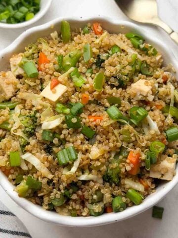 Quinoa fried rice served in a white bowl with spring onions and spoon on the side.