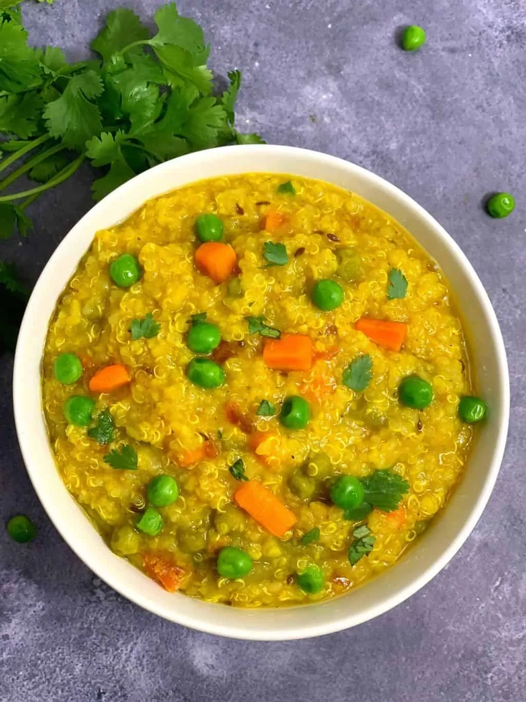 quinoa khichdi served in a bowl with cilantro and green peas on the side