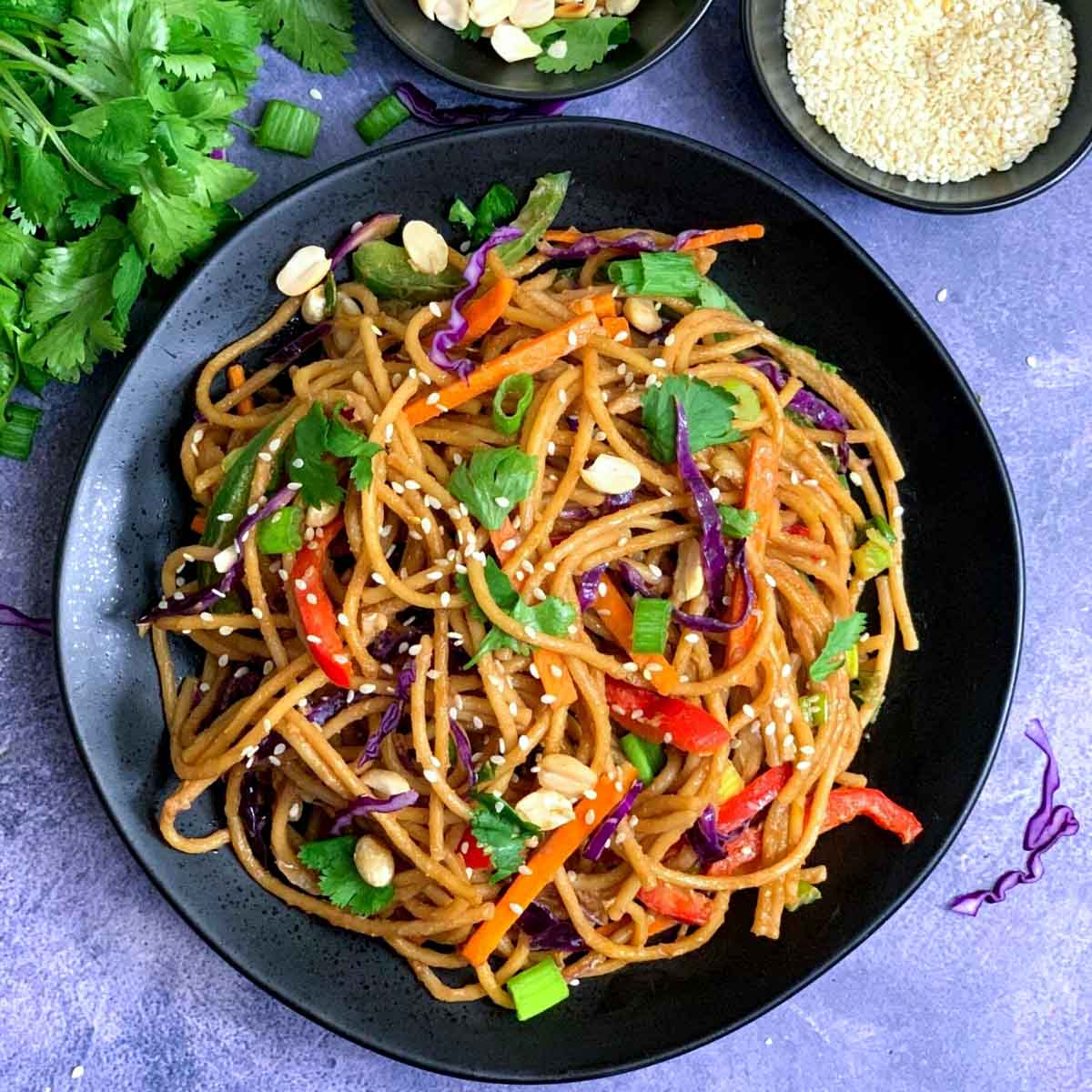 thai peanut noodles served in a black plate with cilantro ,sesame seeds on side