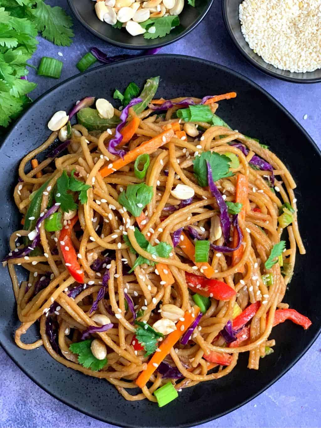 spicy thai peanut noodles made in the instant pot served in a black plate with sesame seeds and roasted peanut on side