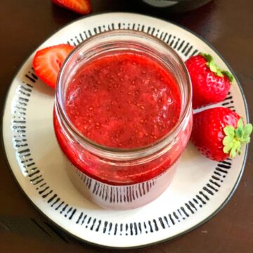 homemade Strawberry Chia Seed Jam in a glass jar with strawberries on the side