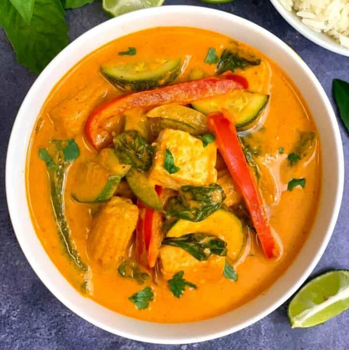 Thai red curry served in a white bowl with lemon wedges and thai basil on side