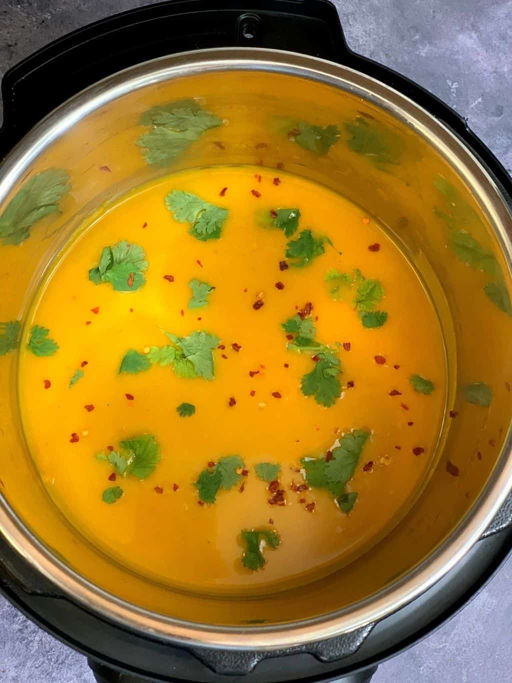 pumpkin curried soup in the pot garnished with cilantro and red chili flakes