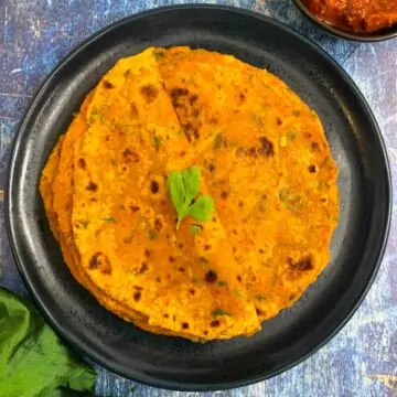 A stack of Tofu Paratha served on a plate with pickle on the side