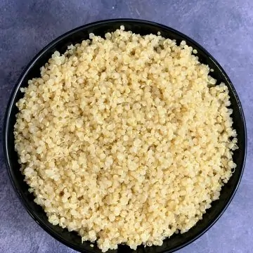 perfectly cooked quinoa in instant pot pressure cooker served in a black bowl and instant pot on side