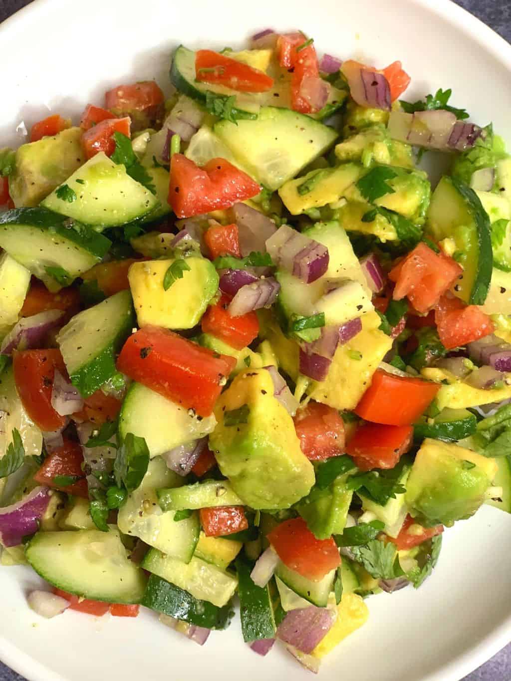 avocado cucumber tomato salad served in a white salad plate