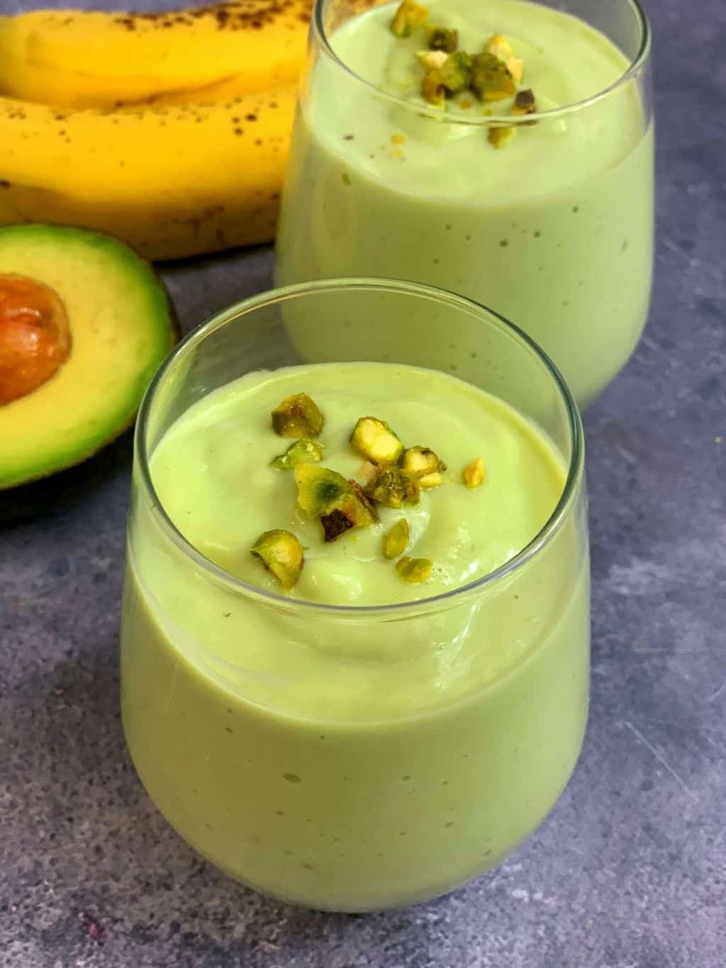 healthy avocado banana smoothie served in a serving glass with avocado and banana on side