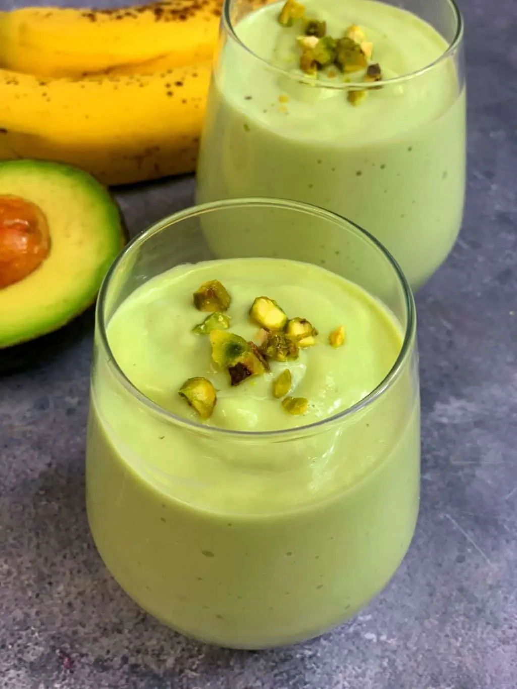 healthy avocado banana smoothie served in a serving glass with avocado and banana on side