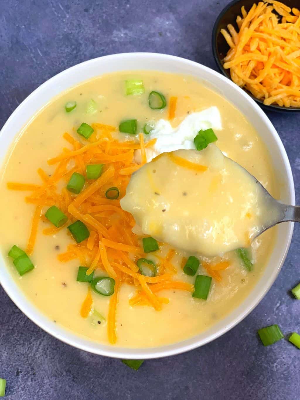 potato soup in a spoon with cheddar cheese on the side