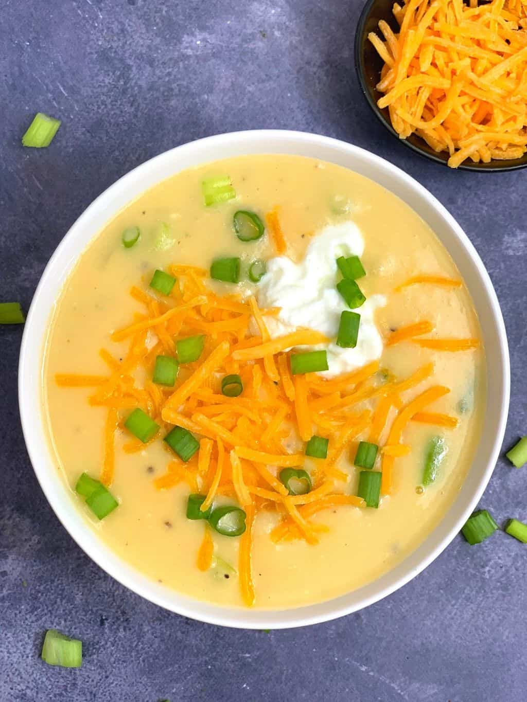 instant pot cheesy potato soup served in a white bowl topped with cheddar cheese and green onions and with side of cheddar cheese