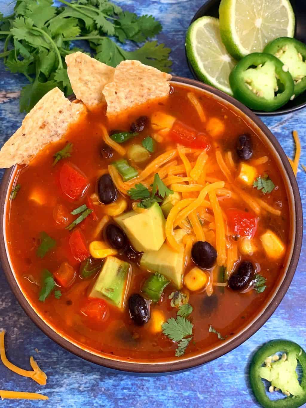 taco soup with black beans served in a bowl with tortilla chips and cheese on the top and lemon wedge jalapeno on the side